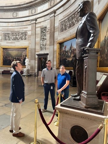 Three college-aged men in business clothing look up at the statue of Ronald Reagan in the U.S. Capitol Rotunda.
