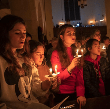 photo of students holding candles in a dark chapel.