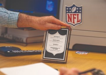 Brian McCarthy holds a plaque that includes information about the National Football League values: integrity, resiliency, respect, and responsibility to team.
