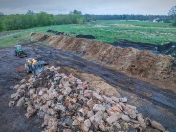 A compositing dump site with two green tractors moving waste.