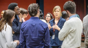 A group of people stands in a circle having a conversation, with one person speaking and gesturing while others listen attentively.