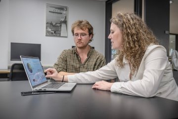 Aam Voter and Lori Clark look at a laptop with data about their food waste reduction effort.