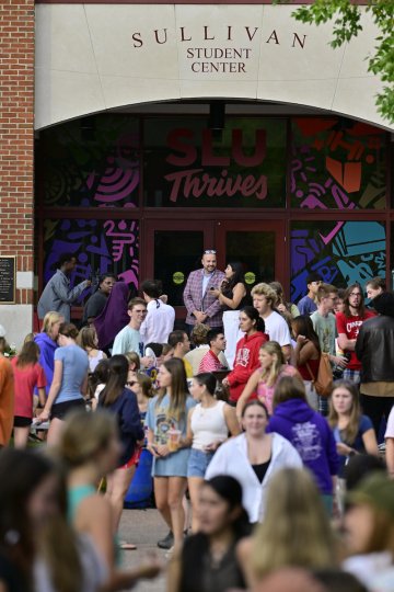 Large group of students gather outside the Sullivan Student Center at Saint Lawrence University, with colorful artwork and the words "SLU Thrives" visible on the glass doors.