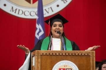 A graduate in cap and gown speaks at the podium during a St. Lawrence University commencement ceremony.