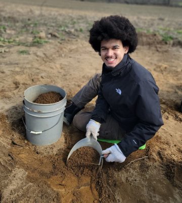 Carlos Sanchez works at a anthropological dig site with a bucket and shovel.