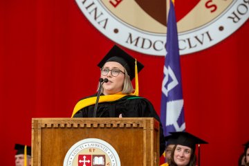 A professor in academic regalia speaks at the podium during a St. Lawrence University commencement ceremony.