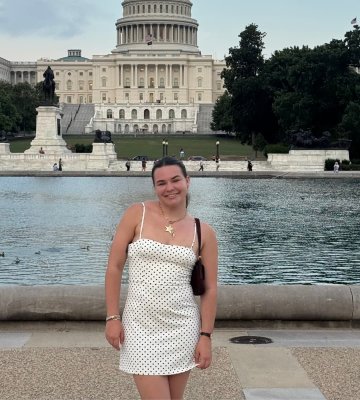 Maggie McNally in a polka dot dress standing in front of the U.S. Capitol.