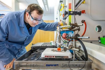 Student researcher wearing safety goggles works with laboratory equipment in a chemistry lab.