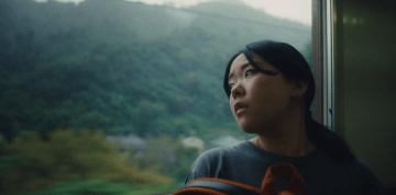 Film still from Chronicle of a City showing a woman looking out a train window.