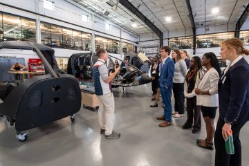 A group of Saint Lawrence students, professionally dressed, gather around Nate Ward as he explains this aviation work.