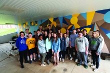 A photo of St Lawrence and Canton Central School students outside of a vibrantly colored mural.