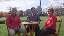 A photo of men and women's hockey team  captains sitting on the quad at a wooden table.