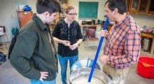 Joe Erilichman and two Saint Lawrence students stand around a large silver bucket brewing beer.
