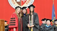 President Kate Morris, Jennifer Curley Reichert and a student stand together, wearing regalia, on the Commencement stage.