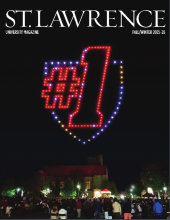 Cover of Saint Lawrence University Magazine showing a nighttime campus scene with a drone light display forming a shield and “#1” above a crowd. The lights glow in red, white, and blue against a dark sky. Text reads “Fall/Winter 2025–26.”